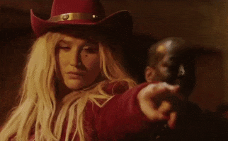 Celebrity gif. Kesha points and curls two fingers at someone, using action cues to tell someone to come here. She looks intimidating, as if ready to tell them off. 