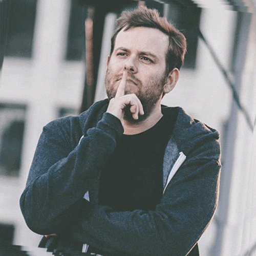 Photo gif. Scruffy man wearing a zip-up hoodie with his index finger resting on his lips, looking contemplative; everything in the photo but his hand rocks left and right.