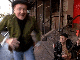 TV gif. Conan O'Brien on Conan wears a top hat and green, striped sport jacket, as he dances on a sidewalk in the city next to a man on a stoop playing a banjo.