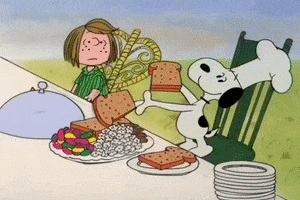 Cartoon gif. Snoopy from A Charlie Brown Thanksgiving wearing a chef's hat cheerfully loads up a dinner plate with snacks: toast, popcorn, pretzel sticks, and jellybeans. Once the plate is properly arranged, he dusts his hands. Not sure what to make of this, Peppermint Patty looks on.