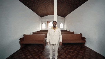 Music video gif. Fireboy DML is standing in a church for his music video for Bandana. He has his hands clasped in front of him as he sings and the camera zooms in closer.