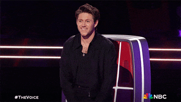 Reality TV gif. Niall Horan, a judge on the "The Voice" Season 23 throws his head back and spreads his arms wide like he's excited and grateful for this performance. 