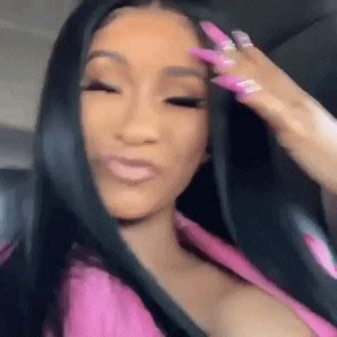 Celebrity gif. Cardi B taking a video selfie in a car while making a duck face and stroking her hair with long pink nails.