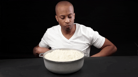 Man sitting at a table in front of an enormous pot of white rice, looking overwhelmed