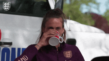 Sports gif. Uniformed Lionesses player sakes a sip of tea out of a mug.
