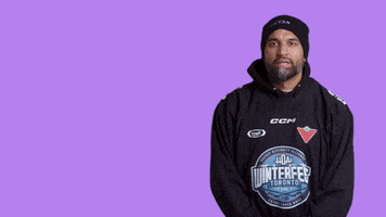 Sports gif. Devan Rajkumar of the Hockey Diversity Alliance stands against a neon purple background wearing a black HDA Winterfest Toronto hoodie and a beanie. He gestures with both hands at us, looking friendly, as he says the text that appears in the frame, "Good morning."