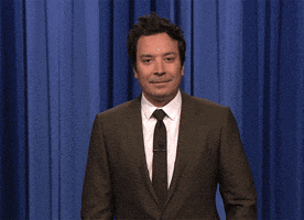 Tonight Show gif. Standing in front of a blue curtain in a black suit, Jimmy Fallon looks around, points at himself, and asks: Text, "Me?"