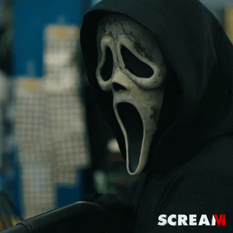 Movie gif. Ghostface from Scream wears a hoodie and holds a black metal weapon pointed off screen, turning his head slowly to look at us in an eerie way. Scream 6 logo at the bottom.