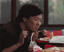Video gif. Ken Jeong leans over a tray of food as milk gushes out of his mouth and onto his hand.