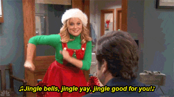 Parks and Recreation gif. Leslie dressed in a Christmas-themed dress and hat, swinging her arms dancing and singing at Ron, "Jingle bells, jingle yay, jingle good for you!" which appears as text.