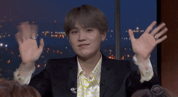 Late Night gif. Min Yoongi of BTS on The Late Show with Stephen Colbert looks at us with a smile as he waves both his hands very fast.