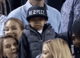 Sports gif. Small child in a crowd respectfully removes his hat, a Jordan x Derek Jeter "RE2PECT" hat, and holds it out.