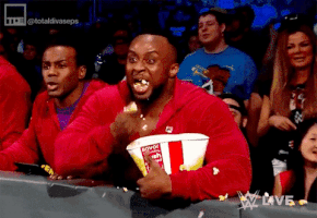 Sports gif. A man in the front row of the audience jumps around with big bulging eyes. He shovels handfuls of popcorn into his already full mouth. Popcorn falls out of his mouth and all over the place.
