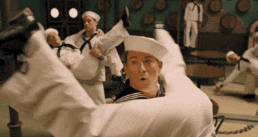 Movie gif. Channing Tatum as Burt Gurney in "Hail, Caesar!" dances in a sailor costume with a group of men. He holds one man upside down, the man's legs splayed wide and his, erm, buttocks in Tatum's face. Tatum looks up from the buttocks with an expression of surprise.