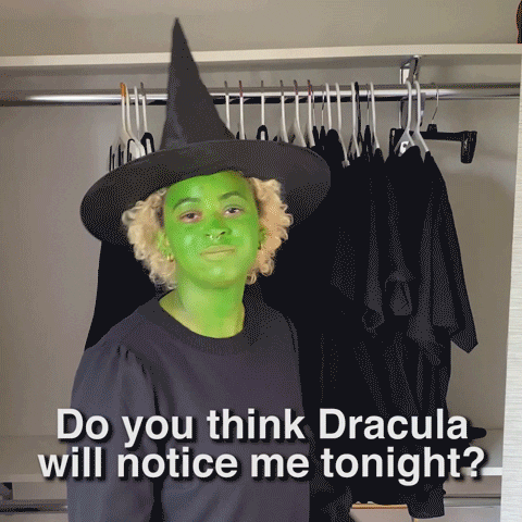 Video gif. Girl dressed as a witch, with green-painted skin, looks at us and says, "Do you think Dracula will notice me tonight?" Another green-painted witch is putting on makeup and turns to grimace and says, "Ew, that guy sucks."
