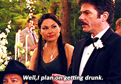 Video gif. A man in a tux at a wedding talks to someone as a woman in a black dress looks up at him and smiles. He says matter of factly, "Well, I plan on getting drunk."