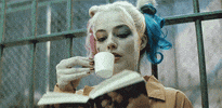Movie gif. Margot Robbie as Harley Quinn reads a book, while sipping a cup of tea that she holds with her pinky out.