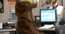 Video gif. A man sits behind a computer in a cubicle and wears a bears costume as he spins around in his chair. Text, "Fur sure."