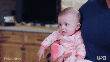 Reality TV gif. Baby on Miz and Mrs. stares blankly and wide-eyed ahead, lips parted.