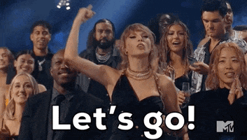 TV gif. Taylor Swift at the 2023 VMAs stands in the audience and pumps a finger high in the air, yelling "Let's go!" as other audience members look out in the same direction as Taylor as they clap and cheer. 