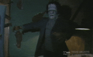 Video gif. Man wearing a Frankenstein mask holds his arms out for balance as he walks through a dark room like he's chasing someone. The video cuts to a low shot of feet walking upstairs away from us. 