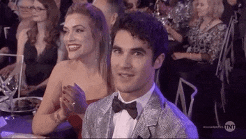 Celebrity gif. Darren Criss sits at a table at the SAG Awards. He looks at us with wide eyes, gritting his teeth nervous, and pulls at collar. People around him clap and laugh.
