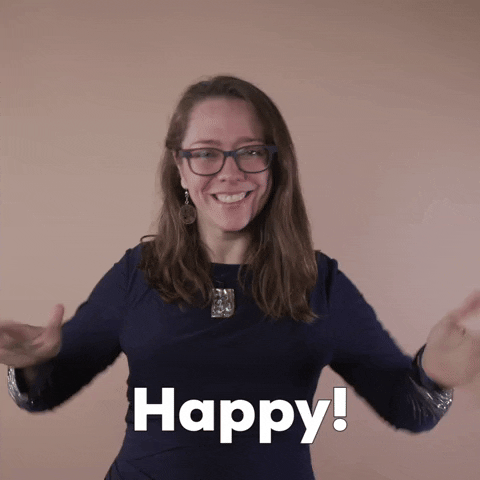 Reaction gif. A Disabled Latina woman with brown wavy hair and glasses dances up and down, smiling broadly and paddling her hands repeatedly at her chest, palms inward, in the ASL gesture for, "Happy."