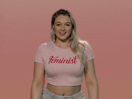 Celebrity gif. Wearing a pink crop T-shirt that says "Feminist," Iskra Lawrence brings both hands to her mouth and blows us a big kiss, opening her arms wide.