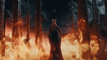 Music video gif. In her video for The Only Heartbreaker, Mitski faces a forest engulfed in flames as she stretches her arms up and spreads her hands out.
