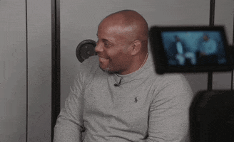 Video gif. Daniel Cormier, a former UFC fighter, is being interviewed as he hears something that makes him laugh. He covers his face with his hand and shakes with laughter.