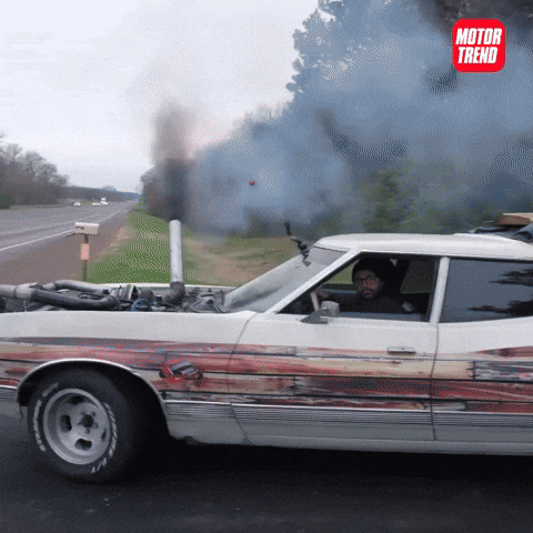 Video gif. Heavily modified car pulls onto and drifts onto a racetrack, black smoke pouring out of a tube linked directly into the exposed engine bay. We then see the car compete in a drag race against a similarly modified car.