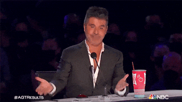 Reality TV gif. On the set of AGT, wearing a black jacket with a half-buttoned white shirt, Simon Cowell turns up his hands in a shrug without looking at us.