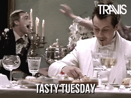 Celebrity gif. Oblivious to a chaotic wedding food fight going on around him, Neil Primrose dips his finger in his dessert and delights in tasting it. Text, "Tasty Tuesday."