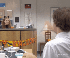 The Office gif. Jenna Fischer as Pam sits at the reception desk air high fiving Jim who is sitting at his desk, air high fiving her back in celebration.