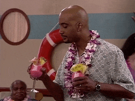TV gif. John Henton as Overton in Living Single. He's on vacation and is on a cruise ship with a flower lei on. He's double fisting two cocktails and he sips on one slowly while raises his eyebrows in satisfaction at the taste.
