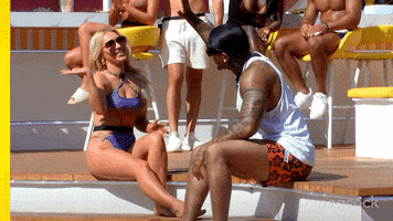 Reality TV gif. Mady McLanahan and Jeff Christian Jr. from Love Island sit alongside the edge of a pool and raise their hands to high five but miss.