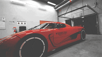 Video game gif. Door of a flashy red Koenigsegg car opens up like a wing and reveals a sleek interior with a dark red steering wheel and a smooth, silver gear system.