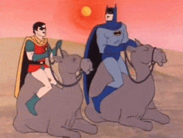 TV gif. Cartoon Batman and Robin sit on camels. They look at eachother and laugh with bouncing shoulders.