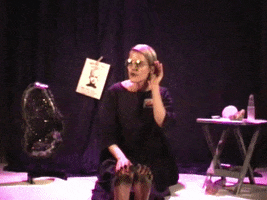 Video gif. A woman sits in the middle of a stage and has her palm up against her ear, attempting to listen to us closely. She listens for a bit then nods and says, "Yes, please."