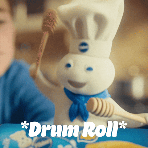 Sponsored gif. The Pillsbury Doughboy, in his iconic blue scarf and Pillsbury chef hat, uses two wooden kitchen tools to drum on a can of Pillsbury Crescent Rolls while a young boy looks on. Text: "*Drum Roll*"