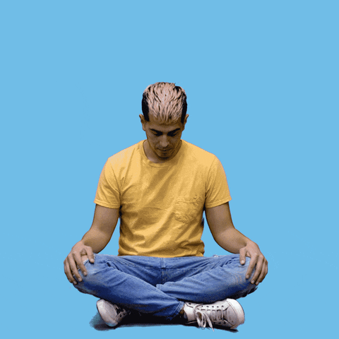 Digital art gif. Man wearing a yellow t-shirt and jeans sits cross-legged with his eyes closed and takes a deep breath. Little cartoon whooshes of air move in and out of his nose as he breathes. White text above the man reads, "Breathe in, breathe out," all against a blue background.