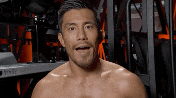 Sports gif. Wrestler Akira Tozawa looks at us with a huge smile, and holds up a thumbs up next to his head as he says, “Good luck!”