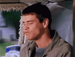 Movie gif. Jim Carrey as Lloyd on Dumb and Dumber rides in a car, chewing on something while smiling and laughing, before his face quickly turns serious.