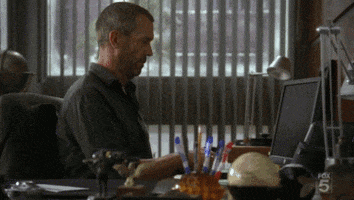TV gif. Hugh Laurie as Dr. Gregory from House sits at a cluttered desk and acts like he's busy by clacking on his computer, which isn't even turned on. He looks up nonchalantly.