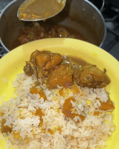 Hands ladling thick chicken curry over a plate of rice in a home kitchen