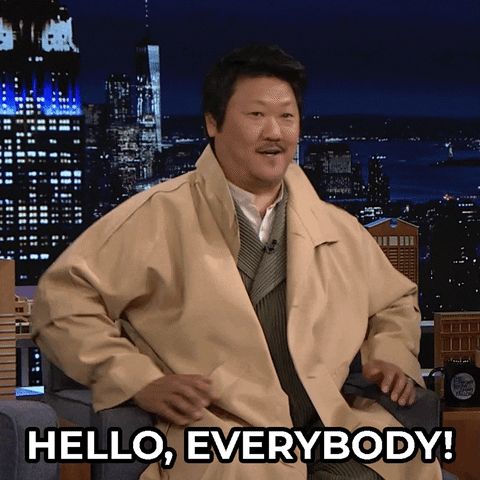 Tonight Show gif. Benedict Wong sits in a seat and waves at the crowd as he says, “Hello, everybody!”