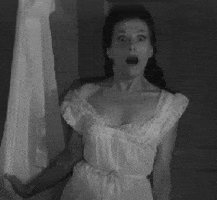 Video gif. Gripping a white curtain for dear life, a woman in a white laced dress sits upright with an expression of pure shock and horror before dropping dead on the ground.