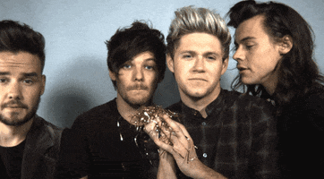 Celebrity gif. Four members of One Direction dramatically throw gold streamers and confetti in slow motion on New Year’s.