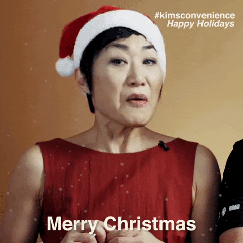 Celebrity gif. Actress Jean Yoon as Umma from Kim's Convenience in a festive red dress and Santa hat and offers holiday greetings with a smile. Text, "Merry Christmas!" 