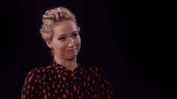 Celebrity gif. Jennifer Lawerence is being interviewed and she clamps her mouth together, trying not to laugh. She fails and she breaks out into laughter, bending forward in her seat.